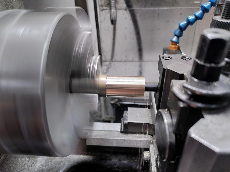 A bronze part viewed side on spinning in a 3 jaw chuck on a lathe. A small boring bar
is disappearing into the center of the part.