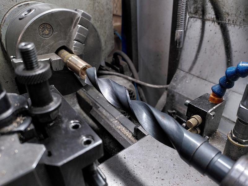 A hollow bronze cylinder is held in the three jaw chuck of a metal
lathe. A large twist drill is held in the tail stock. The drill is wider
than the part.